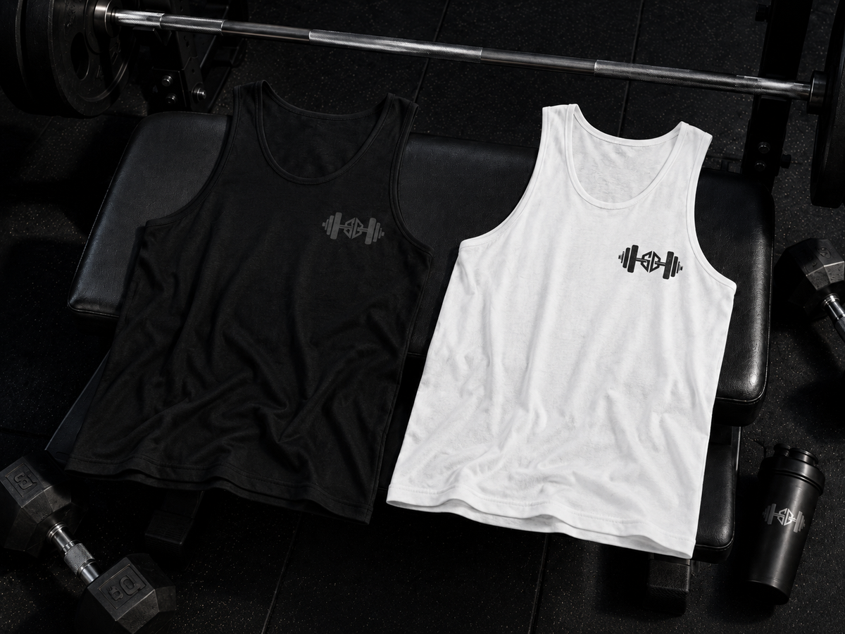 Black and white barbell logo gym tank top laid on a weight bench with dumbbells in a dark weightlifting gym